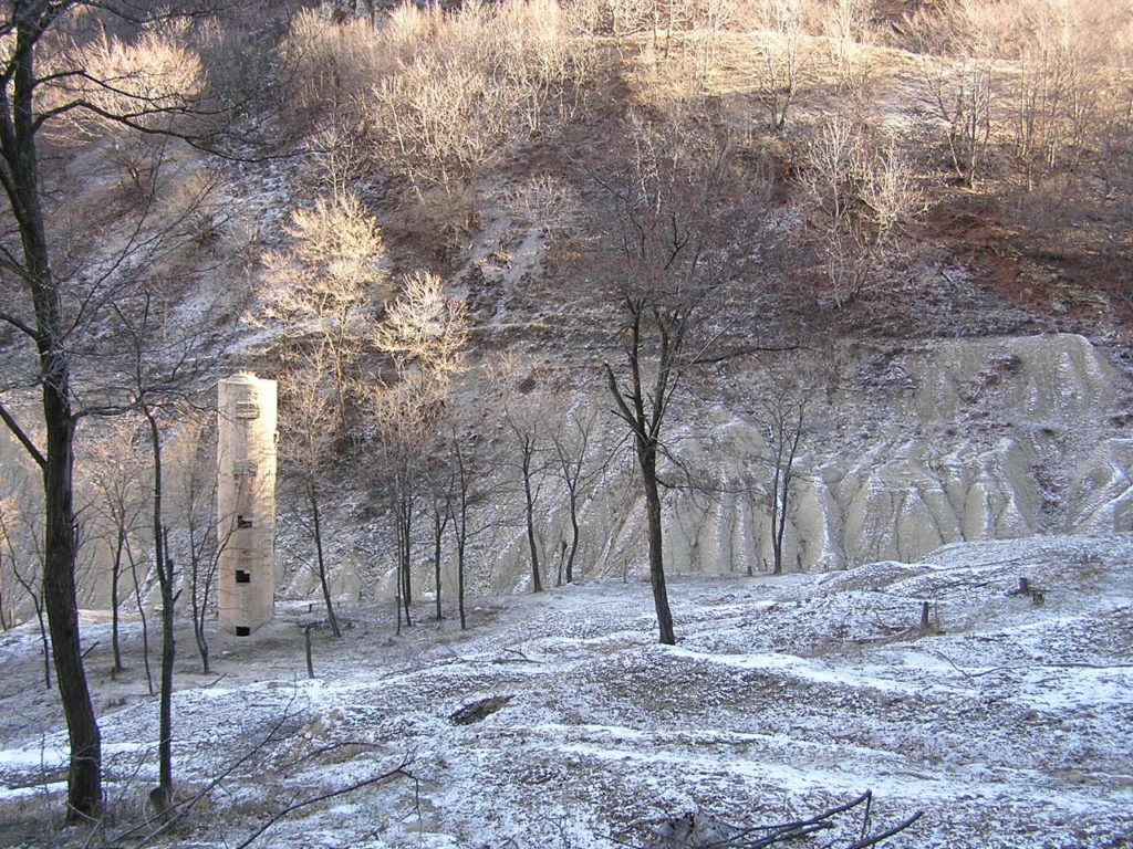 Una delle torri per lo sfioro dell'acqua che si trovava all'interno del bacino, completamente sommersa dai fanghi depositati a decantare che sono defluiti a seguito del crollo. Sullo sfondo alcuni accumuli di fango consolidato.